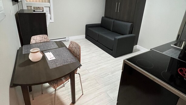 Een knus woongedeelte met een eettafel, een bank, een kitchenette en een raam met zonwering.