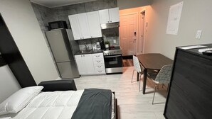 Een kleine hotelkamer met een bed, een bureau, een kitchenette en een eethoek.