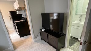 A compact living space with a kitchenette, a flat-screen TV, and a bathroom visible through an open door.