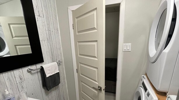 A laundry room with a washing machine, a mirror, and a sink.