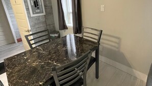 A dining area with a marble table, four chairs, a window with curtains, and a door with a number.