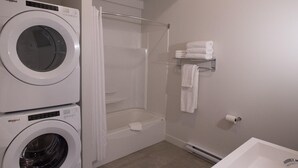 Et vaskerum med to Whirlpool vaskemaskiner, et glas brusekabine, en håndklæderække med foldede håndklæder og en toiletpapirholder på væggen.