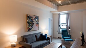 En moderne stue med en grå sofa, et træ sofabord, en blå lænestol og et billede på væggen.