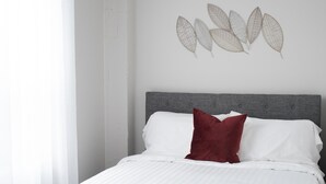 Ein Bett mit weißer Bettwäsche, einem roten Kopfkissen und einem grauen Kopfteil, sowie eine Wand mit blattförmigen Verzierungen.