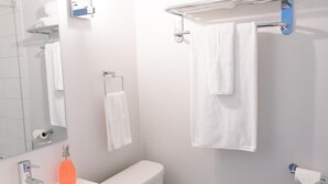Ein modernes Badezimmer mit Waschbecken, Spiegel und Toilette. Am Waschbecken befindet sich ein Handtuchhalter mit zwei Handtüchern und einer Seifenspende.