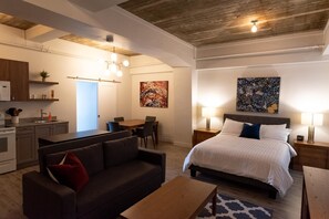 Ein modernes Hotelzimmer mit Bett, einer Sitzecke, einem Couchtisch, einem Schreibtisch und einer Küchenzeile.