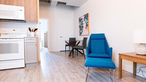 A modern kitchen with white appliances, a dining area with a blue chair, and a painting on the wall. - Suite with closed bedroom on rue Gamble Ouest (Le Central) (Rouyn-Noranda)