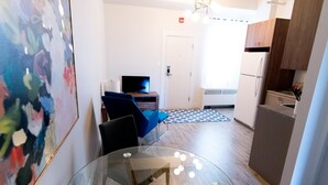 A modern kitchen with a refrigerator, a microwave, and a sink. There is a dining area with a glass table and chairs. - Suite with closed bedroom on rue Gamble Ouest (Le Central) (Rouyn-Noranda)