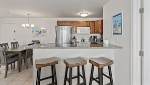 A modern kitchen with a large island, wooden bar stools, and a dining area with a table and chairs.
