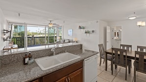 A modern kitchen with a large island, a dining area with wooden chairs, and a view of palm trees through large windows.