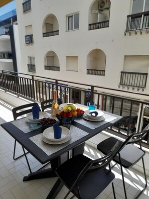 Un balcón con una mesa lista para dos personas, que incluye un frutero, platos y vasos.