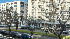 A parking lot with several cars, a building with multiple balconies, and leafless trees.