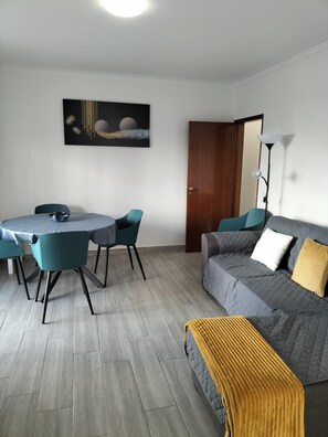 Una sala de estar moderna con un sofá gris, sillas turquesas, una mesa de comedor redonda y un cuadro de cuerpos celestes.