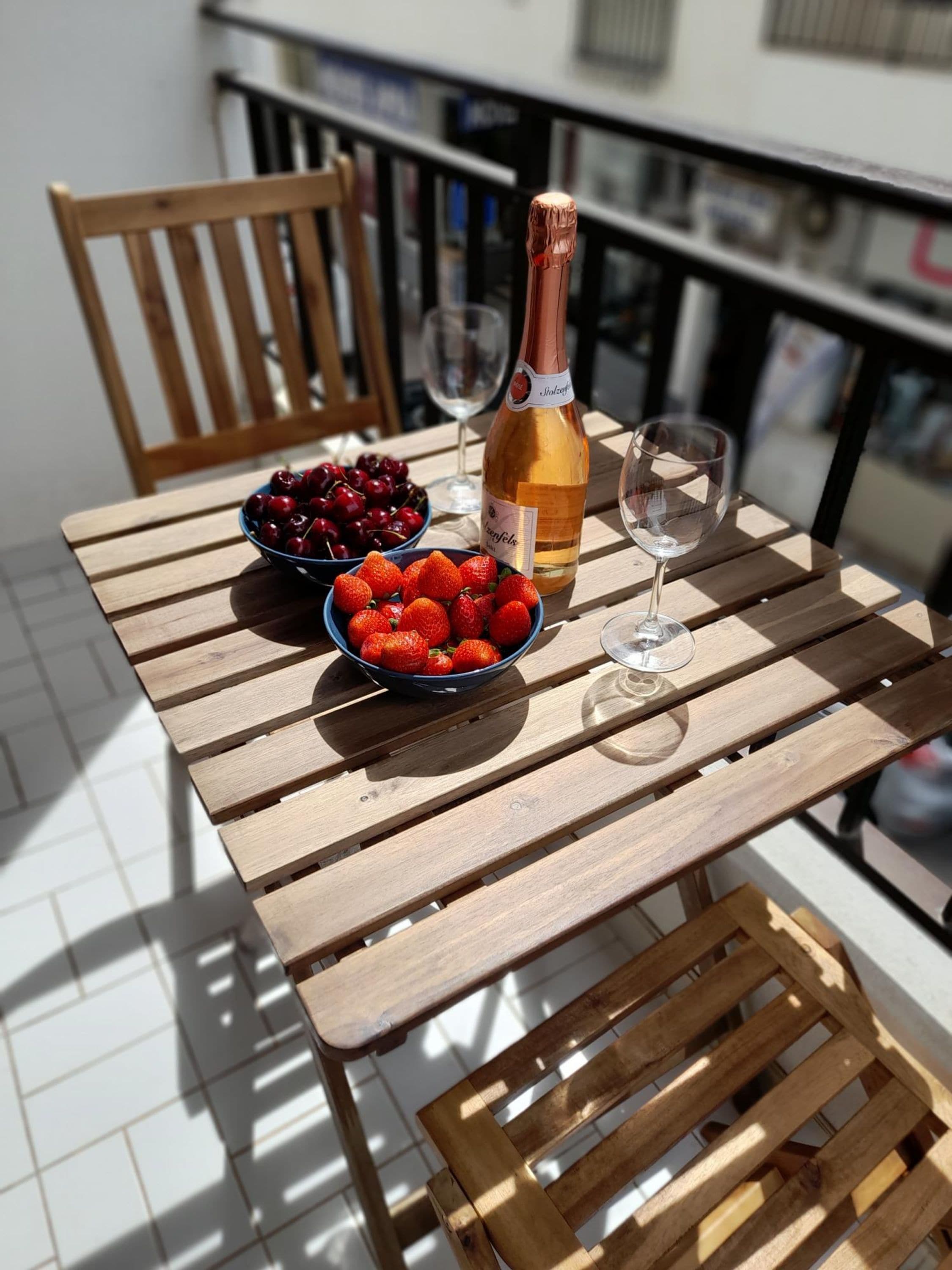 Een houten tafel met een fles wijn, een schaal aardbeien en een schaal kersen.
