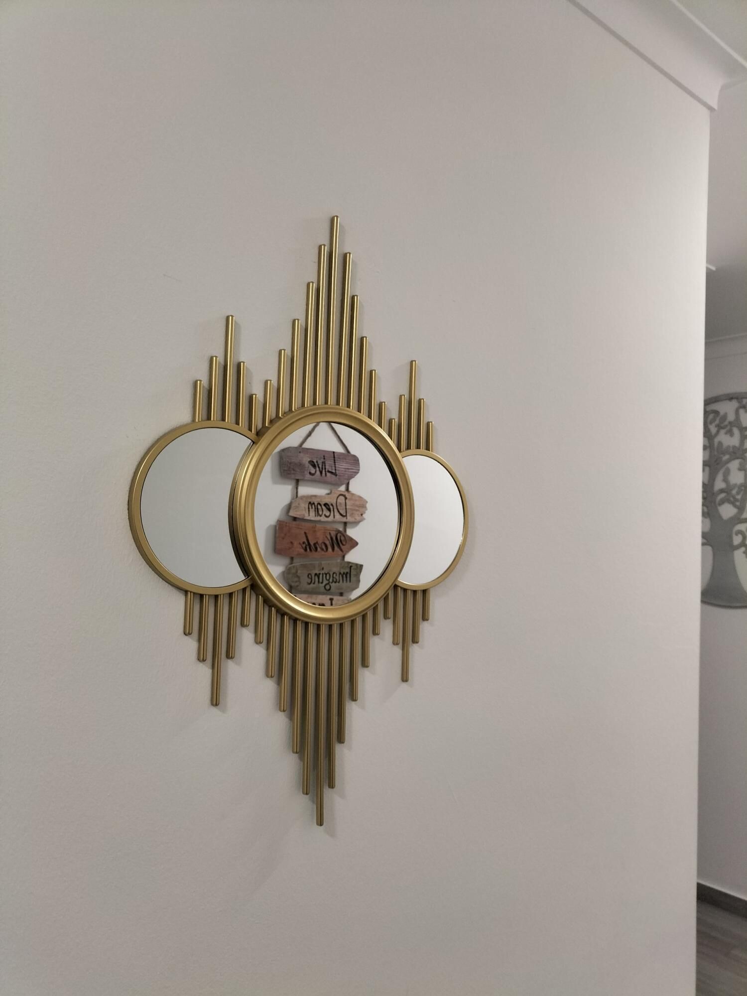 Un adorno de pared con tres espejos y un espejo circular central rodeado de letreros de madera.