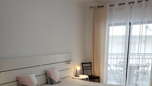 A bedroom with a bed, bedside table, chair, and a view of the outside balcony.
