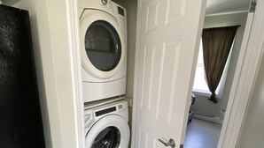 A laundry room with two stacked front-loading washers and dryers, a black refrigerator, and a white door leading to another room. - Two bedrooms flat in Rouyn (Le Cardinal) (Rouyn-Noranda)