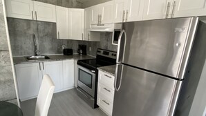A modern kitchen with white cabinets, stainless steel appliances, and a round dining table. - Two bedrooms flat in Rouyn (Le Cardinal) (Rouyn-Noranda)