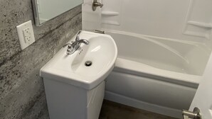 A bathroom with a white sink, a bathtub, and a shower. There is a mirror above the sink and a light fixture above the shower. - Two bedrooms flat in Rouyn (Le Cardinal) (Rouyn-Noranda)