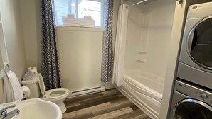 Une salle de bain avec des toilettes, un lavabo et des piles de serviettes près de la fenêtre.