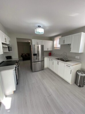 A modern kitchen with white cabinets, stainless steel appliances, and a light wood floor. - Three bedrooms flat in Rouyn (Le Cardinal) (Rouyn-Noranda)