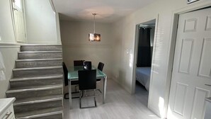 Une cuisine compacte avec un coin repas, un escalier et une horloge au mur.