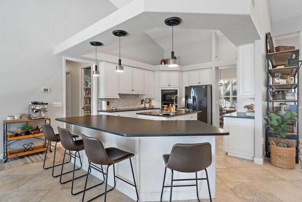 A modern kitchen with a central island, bar stools, pendant lighting, and white cabinetry. - Private, tranquil 4 bed retreat near Crystal River (Lecanto)