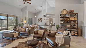 Un salón espacioso con muebles de cuero, una amplia estantería y vistas al exterior.