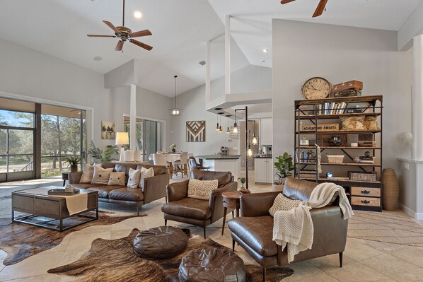 A spacious living room with leather furniture, a large bookshelf, and a view to the outside. - Private, tranquil 4 bed retreat near Crystal River (Lecanto)