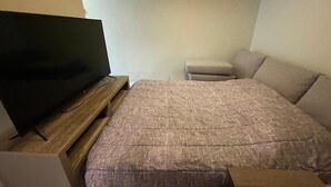Une chambre à coucher avec un lit, un téléviseur posé sur un meuble en bois, une petite table et un luminaire au plafond.