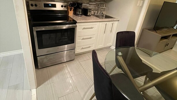 Une cuisine moderne avec des meubles blancs, des appareils en acier inoxydable, une table à manger en verre et un téléviseur à écran plat.