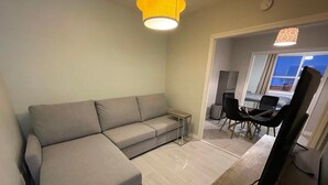 Un salon moderne avec un canapé d’angle gris, une petite table et un coin repas avec des chaises.