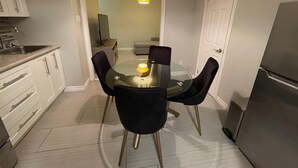 Une cuisine compacte avec une table ronde en verre, quatre chaises noires, un réfrigérateur moderne et des meubles de cuisine blancs.