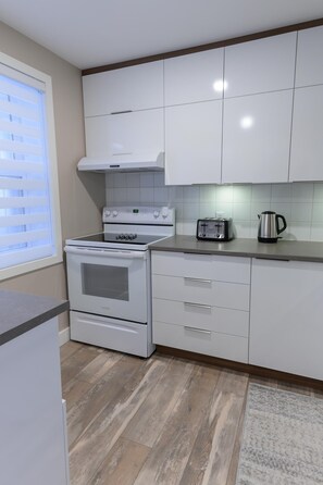 A modern kitchen with white cabinets, a built-in oven, a toaster, and a kettle.