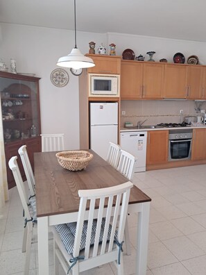 Eine moderne Küche mit Holzschränken, einer Mikrowelle, einem Kühlschrank und einem Esstisch mit Stühlen.