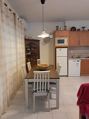 Un coin repas avec une table en bois, des chaises blanches, un panier en osier et un luminaire suspendu.