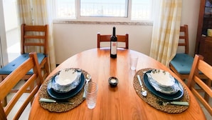 Una mesa de comedor con una botella de vino, dos platos y cubiertos, ubicada en una habitación con vista al mar a través de una ventana.