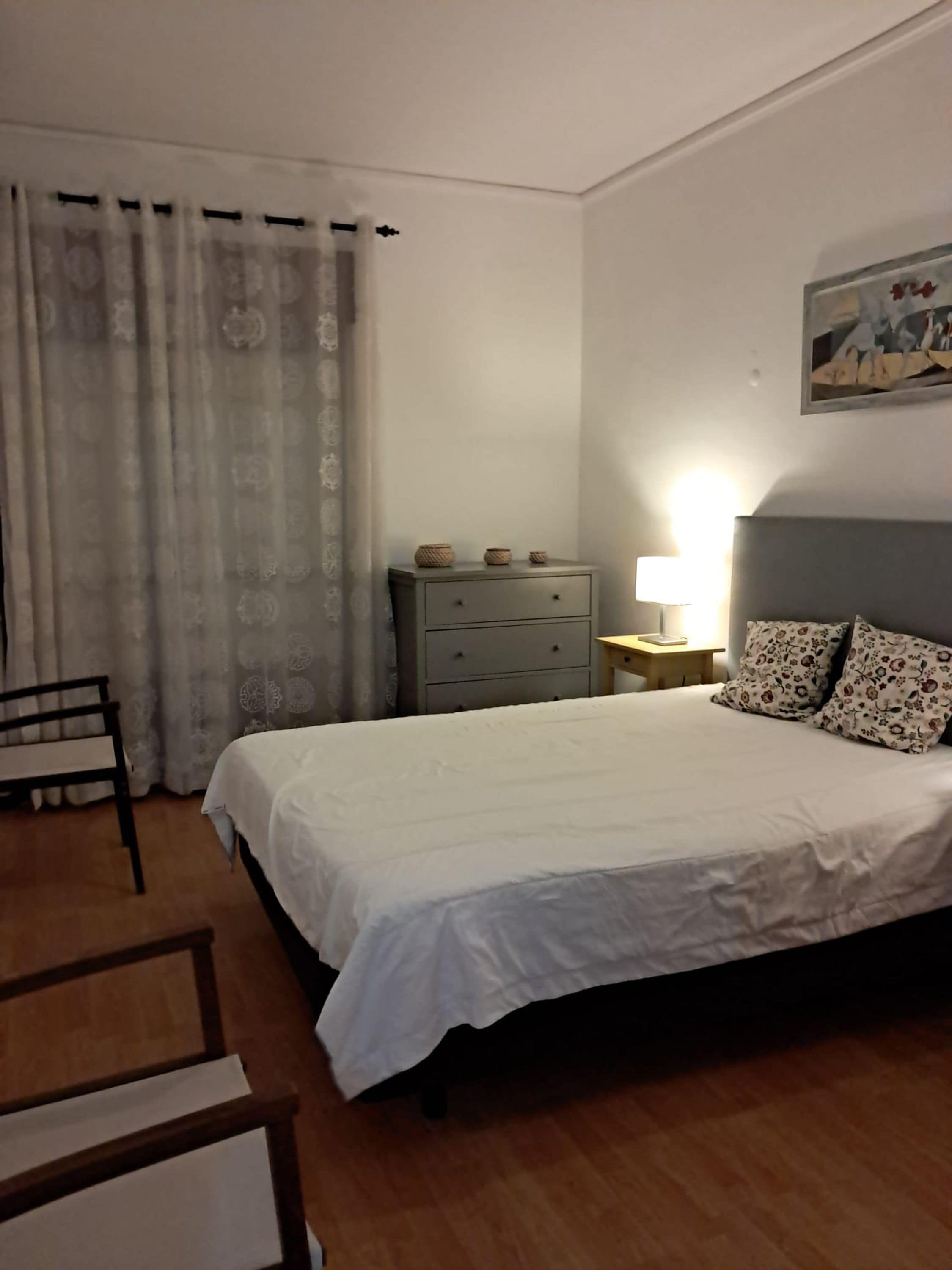 Una camera da letto con un letto, un comodino, una lampada, una cassettiera e una sedia.