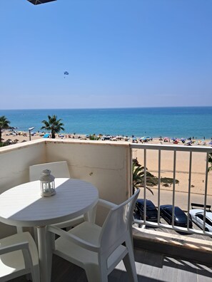 A balcony with a table and chairs, overlooking a beach with umbrellas and people. - T2-mama II AC Frente MAR (Loulé)