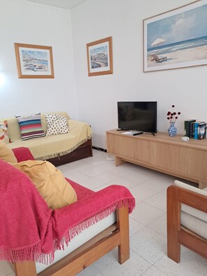A living room with a sofa, a TV, and a coffee table. There are framed pictures on the wall. - T2-mama II AC Frente MAR (Loulé)
