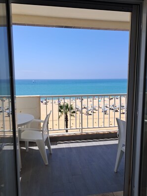Un balcon donnant sur une plage, avec des chaises blanches et une table.