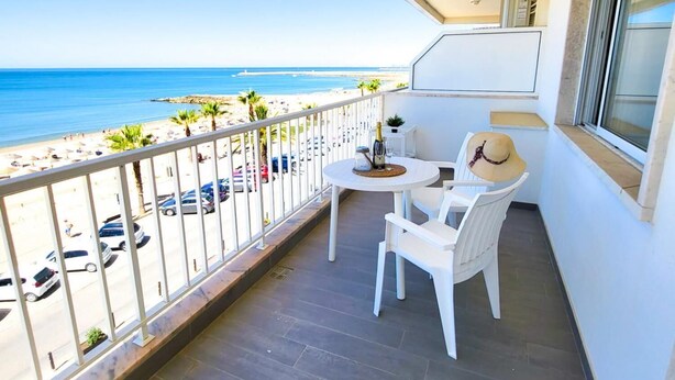 Un balcón con vista a la playa, una mesa con sillas y una botella de champán.