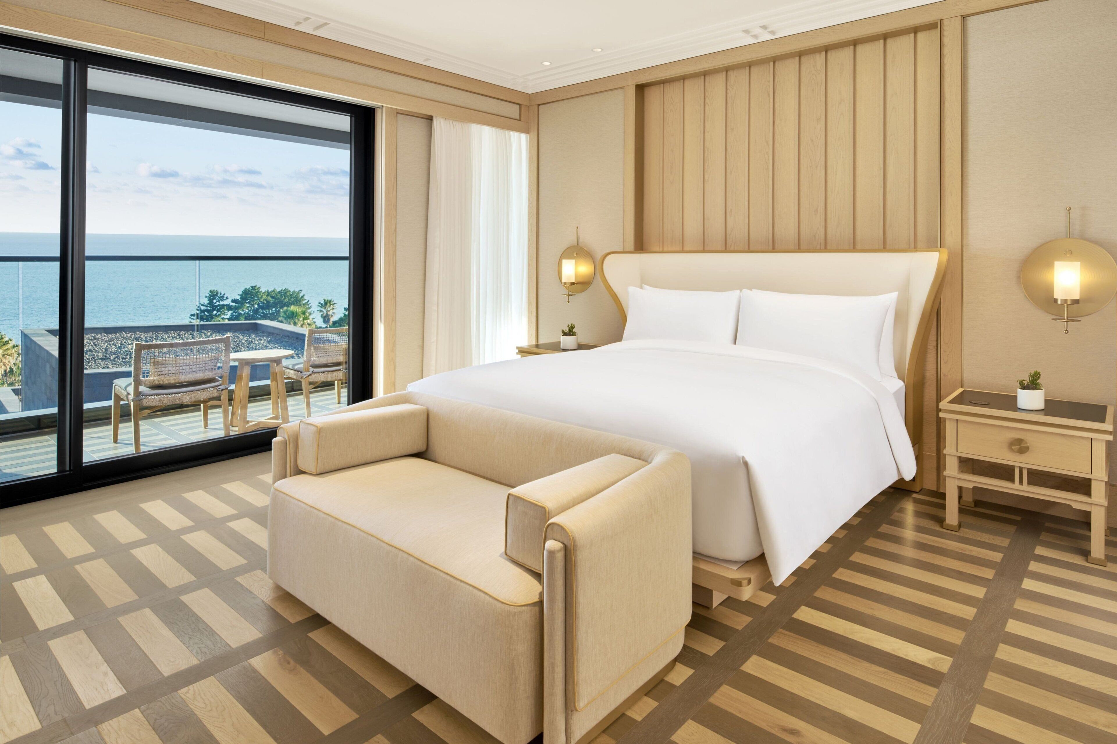 A hotel room with a large bed, a sofa, a small table, and a view of the sea.