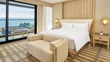 A hotel room with a large bed, a sofa, a small table, and a view of the sea.