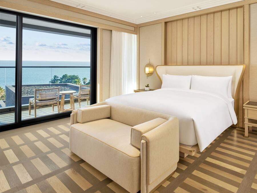 A hotel room with a large bed, a sofa, a small table, and a view of the sea.