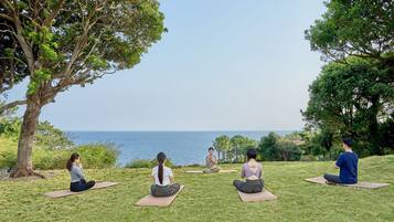 A group of people sitting on yoga mats outdoors with a view of the sea.