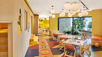 A brightly colored children's playroom with wooden furniture, a colorful play mat, and large windows offering a view of the outdoors.