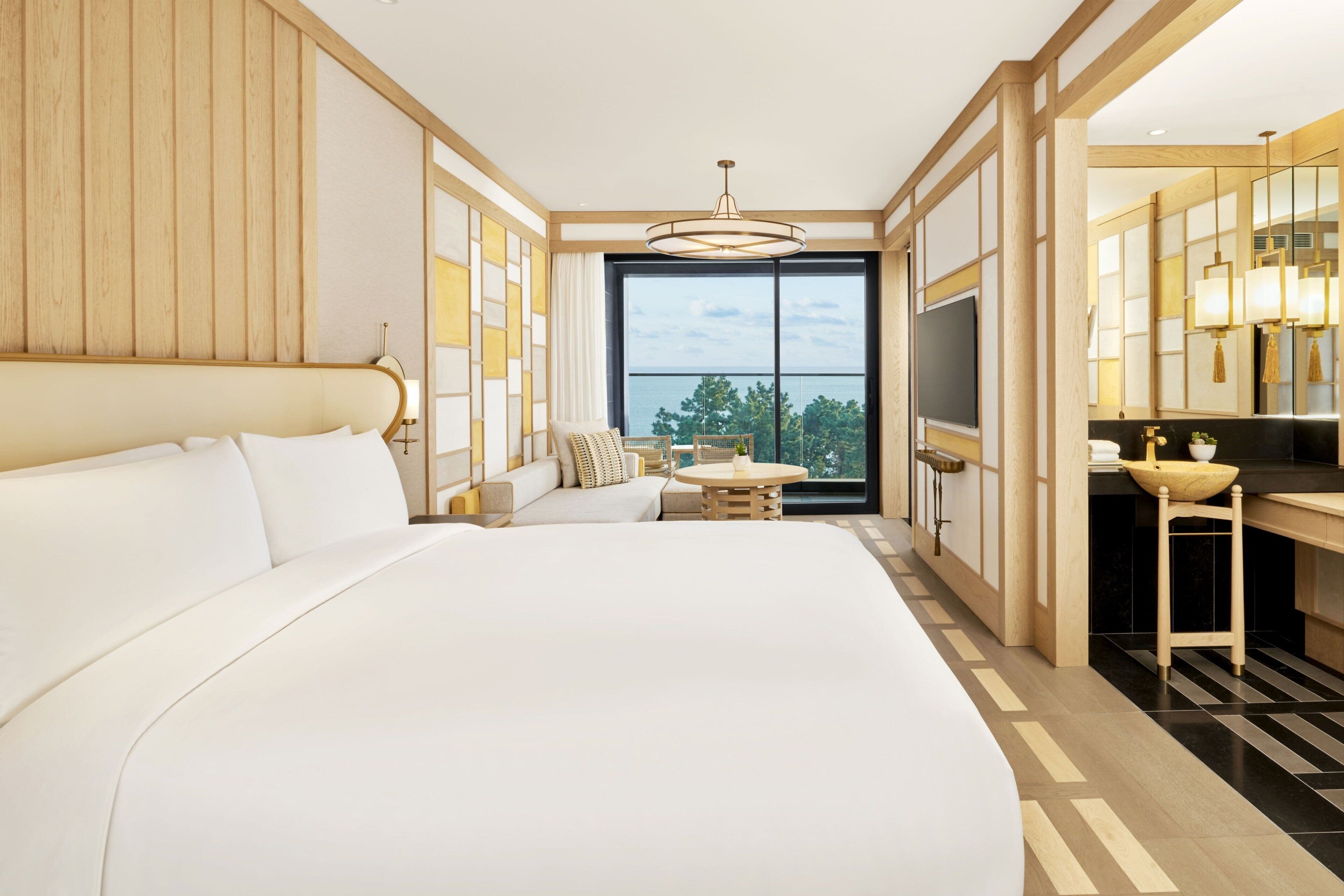 Una habitación de hotel moderna con una cama grande, un pequeño rincón de descanso, una mesa de comedor y vistas al exterior.