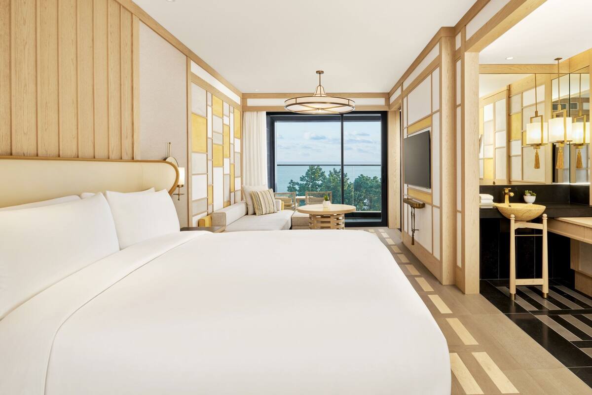 Una habitación de hotel moderna con una cama grande, un pequeño rincón de descanso, una mesa de comedor y vistas al exterior.