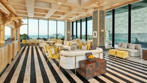 Een ruime lounge met een zwart-wit gestreepte vloer, grote ramen met uitzicht op de zee, en diverse zitopstellingen, waaronder banken en stoelen.